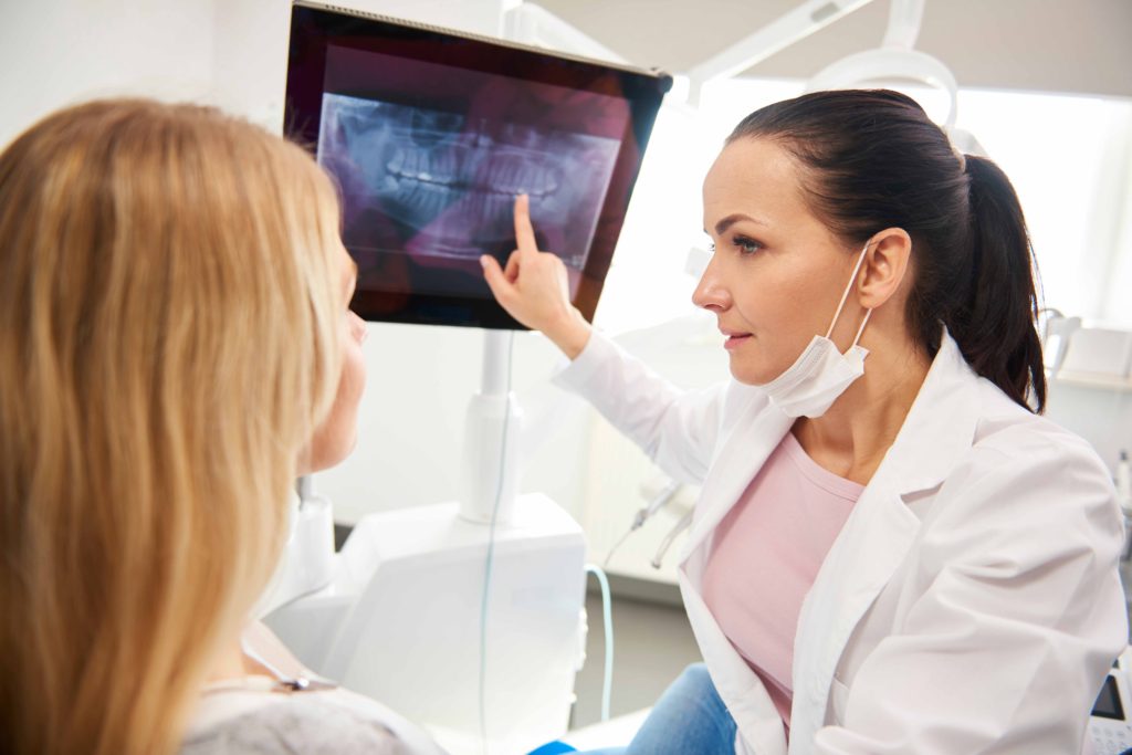 レントゲン写真を指差しながら説明している女性歯科医師と説明を聞く女性患者